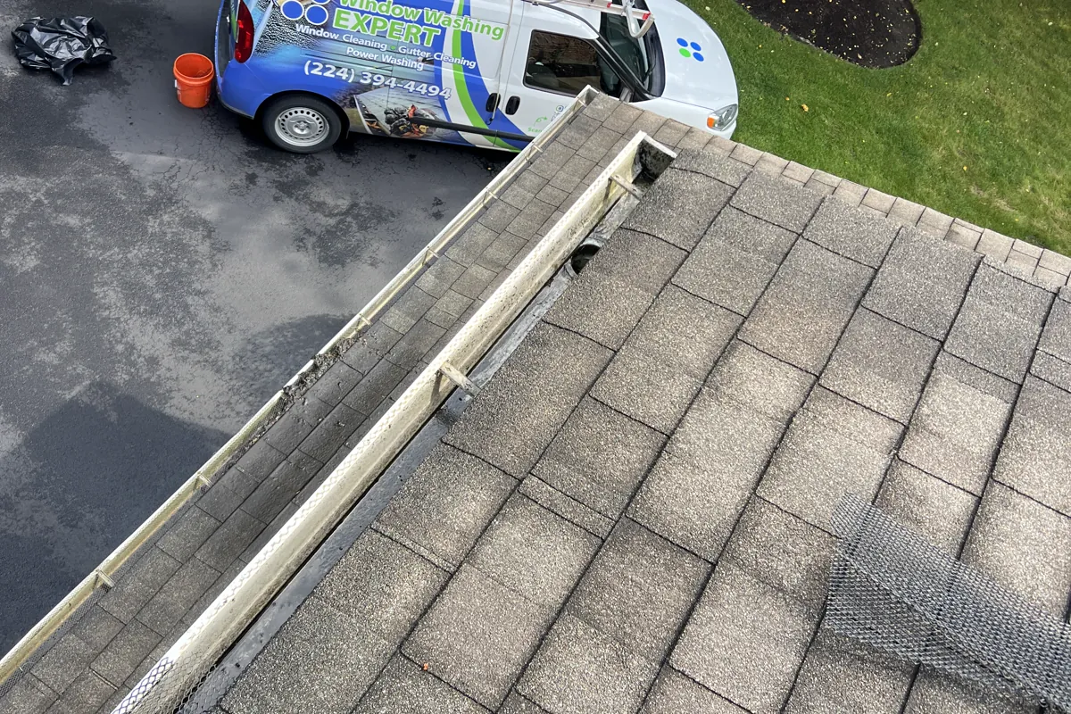 After gutter guard cleaning on a two-story Libertyville home: the cleared gutter along the roofline, a screen guard panel resting on the shingles, and the Window Washing Expert van in the driveway