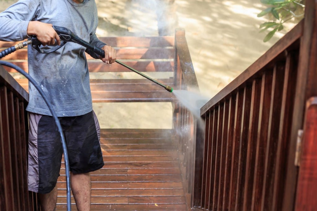 man pressure washing wooden staircase outside